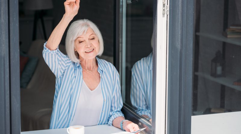 mujer adulta mayor asomada en la ventana con un periódico en la mano y una taza de café